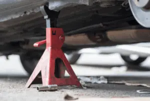 Properly positioned safety jack stand required for safe vehicle elevation during brake bleeding procedure Red safety jack stand supporting vehicle undercarriage at designated lift point for secure brake service access